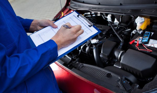 Mechanic Holding Clipboard In Front Of Open Car Engine